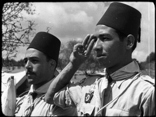 Arab Scouts, types from all Arab countries [saluting boy scout and leader wearing fez-type caps] [picture] / [Frank Hurley]