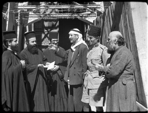 Greek Service in Holy Sepulchre [group of six men, including priests, in conversation] [picture] / [Frank Hurley]