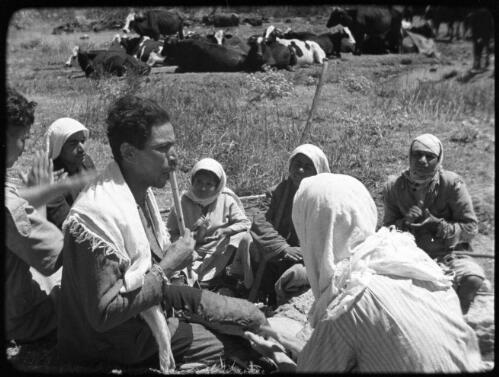 Huleh [Palestine, small group of seated women listening and clapping to shepherd with flute, with a herd of cattle in background, 2] [picture] / [Frank Hurley]
