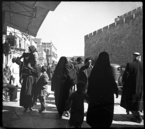 [Street scene adjacent to city wall, with men, women and children, sidewalk cafe, Old City, Jerusalem] [picture] / [Frank Hurley]