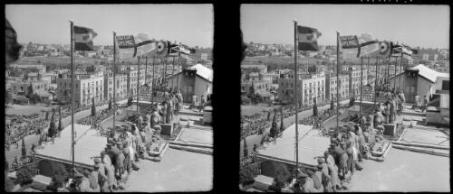 Sundry stereos, Jerusalem [view from rooftops of crowd gathering along main street with flags flying from masts atop roof] [picture] / [Frank Hurley]