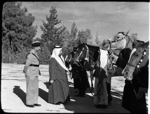 Emir [dignitary in Arab headdress inspecting a parade of men and horses, officer looking on] [picture] : [Jordan] / [Frank Hurley]