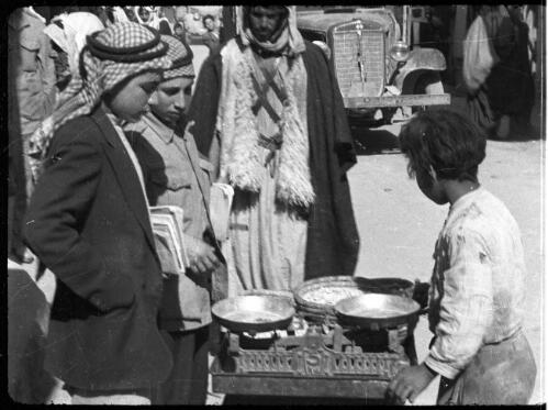 Transjordan film clips, Amman [man and three children assemble around some scales] [picture] : [Jordan] / [Frank Hurley]