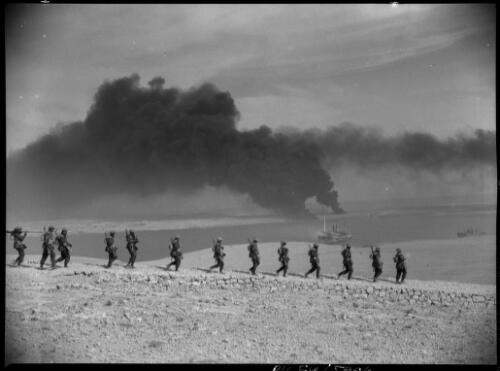 [Tobruk burns in the background as Australian troops rest on the heights overlooking the coastal town, before advancing to occupy it,  January 1941] [picture] : [Barqah, Libya] / [Frank Hurley]