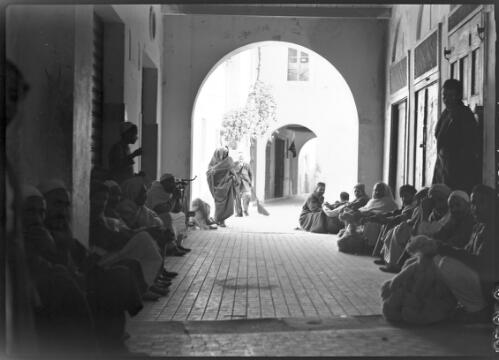 [Arcade with people waiting, man in the background holding a broom, ca. 1940-1946] [picture] : [Barqah, Libya] / [Frank Hurley]