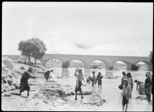 [Group of people in the river shallows, a bridge in the background] [picture] : [Iran, World War II] / [Frank Hurley]