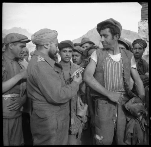 [Numerous male personnel standing around watching one man inject another in the arm via syringe, World War II, 2] [picture] : [Iran] / [Frank Hurley]