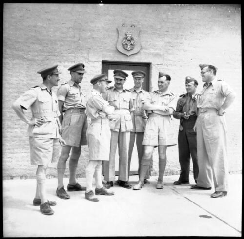 [Eight male military personnel standing in front of a closed door, emblem above the door frame reads REME (Royal Electrical and Mechanical Engineers?), World War II] [picture] : [Iran] / [Frank Hurley]