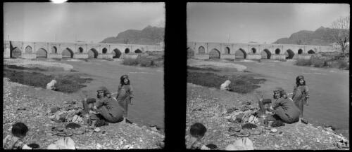 [River scene including a woman crouched beside a basin washing cloths with a child standing beside her, World War II] [picture] : [Iran] / [Frank Hurley]