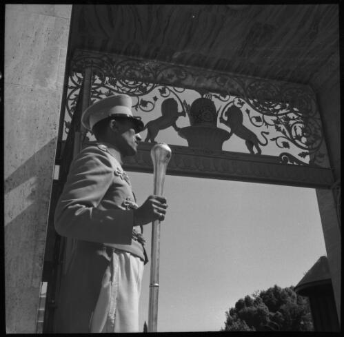 Sunday shots, Iran [guard or doorman above whom is an elaborately decorated coat of arms that shows two lions, holding swords, flanking a central structure, World War II] [picture] : [Iran] / [Frank Hurley]