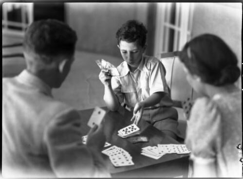 Feisal enjoys a simple game of cards, Miss Ramirez is his Governess & Mr Sidebottom his physical instructor [picture] : [Iraq, World War II] / [Frank Hurley]