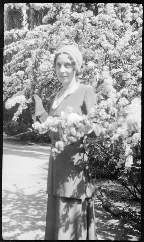 [Unidentified woman standing between branches with blossoms on] [picture] / [Frank Hurley]