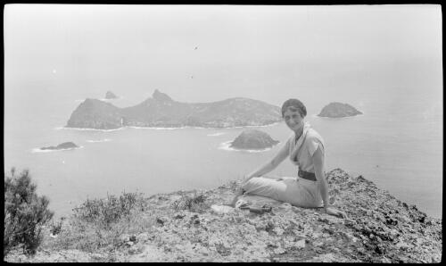 [Unidentified woman sitting on a rock with Roach Island in the background, Lord Howe Island, 2] [picture] / [Frank Hurley]
