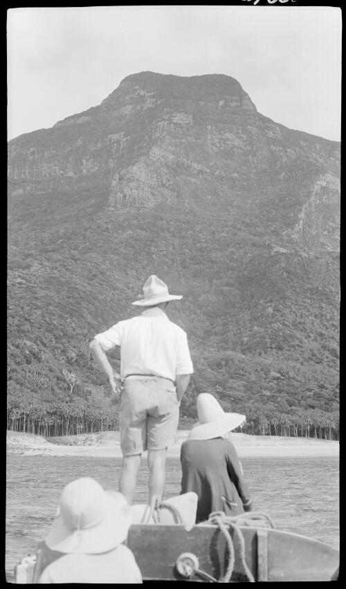 [Unidentified man standing on the end of a boat with two unidentified women sitting beside and behind him, Lord Howe Island, 1] [picture] / [Frank Hurley]