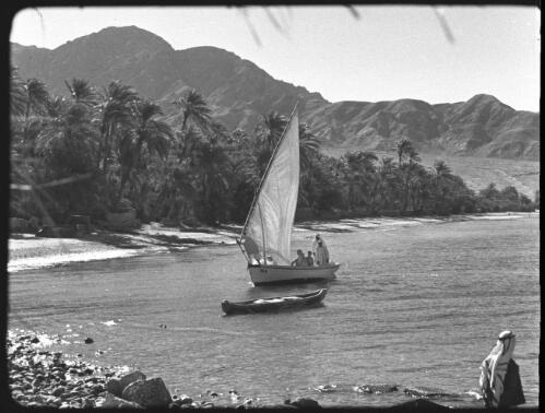 Aquaba, Jordan [felucca sailing in front of palm trees, man in foreground] : [Trans-Jordan, World War II] [picture] / [Frank Hurley]