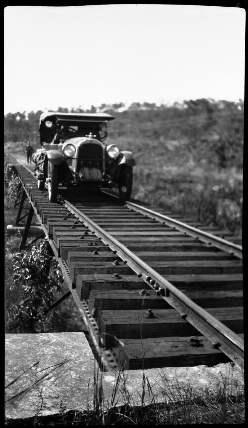 Crossing flooded country between Pine Creek and Darwin, June 1925 [motor vehicle on railway track, 1] [picture] : [Central Australia] / [Frank Hurley]