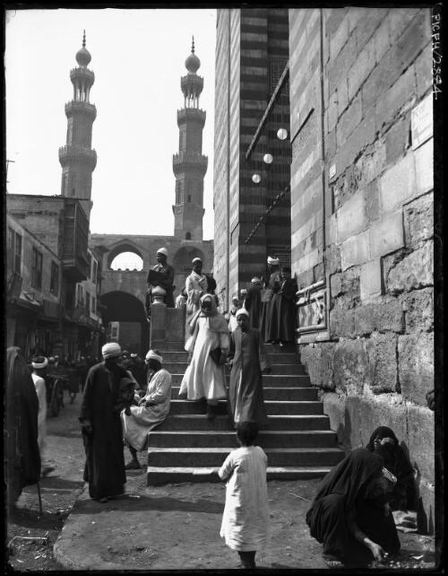 [Figures on the steps of a mosque or a gate with twin minarets and stripes, Cairo] [picture] : [Cairo, Egypt, World War II] / [Frank Hurley]