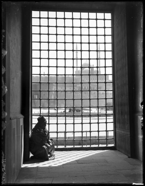 [Kneeling figure with view of mosque through grille] [picture] : [Cairo, Egypt, World War II] / [Frank Hurley]