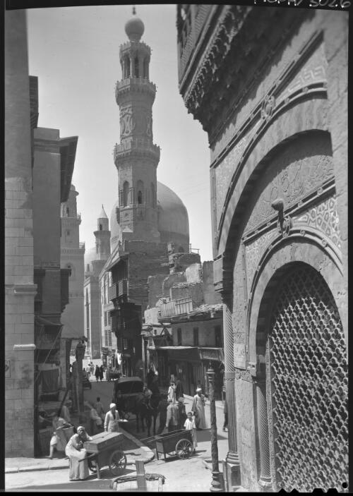 Mosque in foreground is Sultan Barquq Centre En Nasir Mahommed & in distance Mosque of Qalaun (1284AD) [with figures, handcarts and animals in a narrow street] [picture] : [Cairo, Egypt, World War II] / [Frank Hurley]