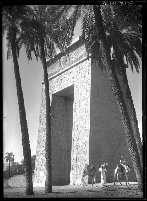 [Gate or archway with bas relief sculpture and palm trees and figures with camels] [picture] : [Egypt, World War II] / [Frank Hurley]