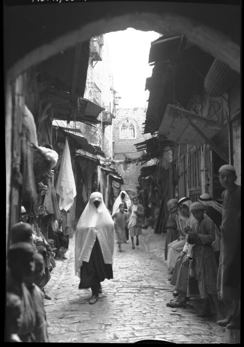 [Narrow street scene showing children and women wearing veils, facing the camera] [picture] / [Frank Hurley]