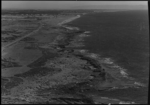 [Large expanse of water or sea on right side, with raised road, track or railway line on left] [picture] / [Frank Hurley]