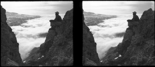 Lebanon landscape, clouds drifting & filling up Wady Quadisha [lone figure on rocky outcrop overlooking the scene] [picture] : [Lebanon, World War II] / [Frank Hurley]