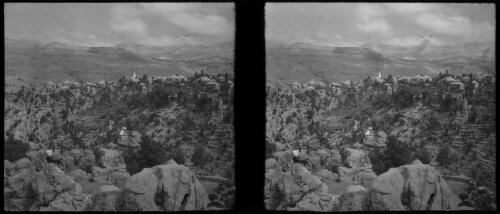 In the Lebanons [seven seated figures pose on rocks with a hillside village in the background] [picture] : [Lebanon, World War II] / [Frank Hurley]