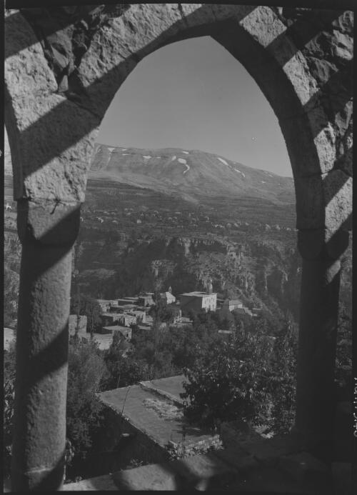 [Elevated view of distant hills and village rooftops framed in the arch of a building] [picture] / [Frank Hurley]