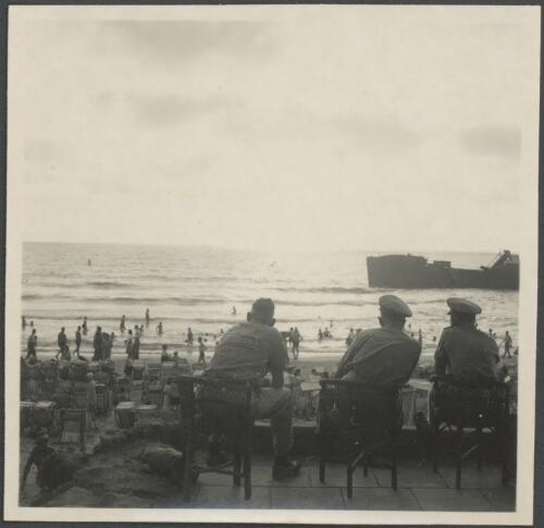 [Three seated military figures overlooking Tel Aviv beach, ship in outlying waters, 1] [picture] / [Frank Hurley]