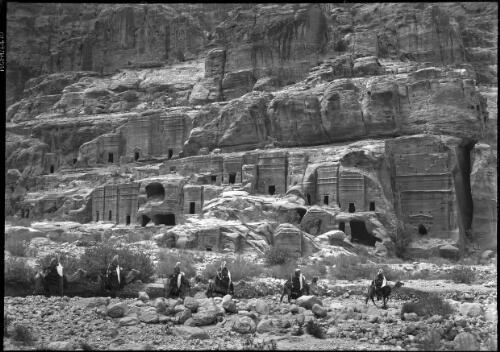 [The Street of Facades, comprising over 40 Nabatean tombs and houses, six men on camels in foreground] [picture] : [Petra Valley, Jordan] / [Frank Hurley]