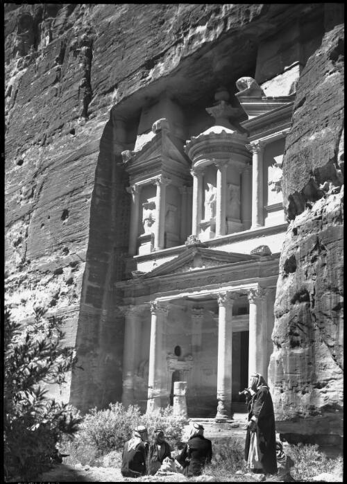[Facade of El Khazne, four figures in foreground, one smoking pipe] [picture] : [Petra Valley, Jordan] / [Frank Hurley]