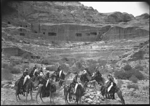 Petra, the great amphitheatre carved from a mountain face with a seating capacity of 3000 [men on camels] [picture] : [Petra Valley, Jordan] / [Frank Hurley]