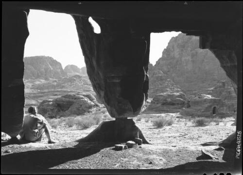 Petra valley [figure resting under arch of excavated tomb] [picture] : [Petra Valley, Jordan] / [Frank Hurley]