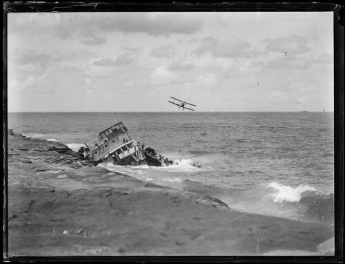 Biplane flying over a ship wrecked on the rocks, New South Wales, ca. 1930s [picture]
