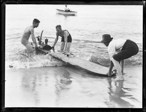 Three men launching a motorised surfboard used for lifesaving, New South Wales, 14 January 1932 [picture]