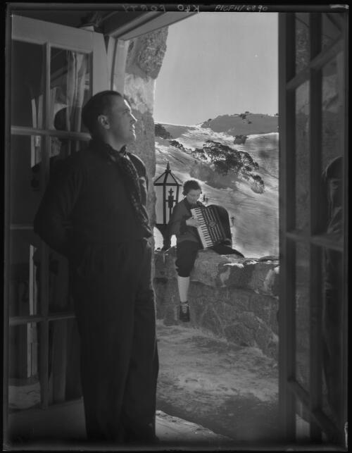 [Mrs Mitchell playing piano accordion] with Toni Mitchell standing at door [Charlotte Pass] [picture] : [Kosciuszko, New South Wales] / [Frank Hurley]