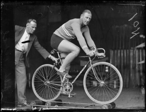 Bobby Pearce training for the Empire Games on his Malvern Star bicycle with assistance from a man, New South Wales, 24 June 1930 [picture]
