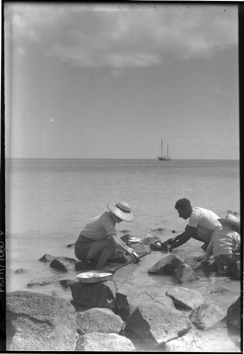 [Man, woman and child, with fresh fish and frypan, boat in distance, 1] [picture] : [Manly, New South Wales] / [Frank Hurley]