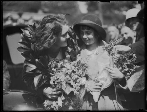 Swimmer Clare Dennis wearing the laurels of victory and holding flowers with a young girl after arriving in Circular Quay, Sydney, 15 September 1932 [picture]