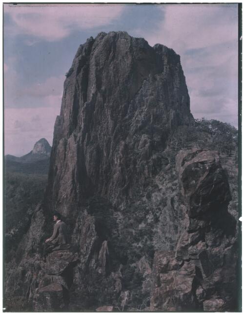 [A man seated by Crater Bluff, smoking a cigarette] [picture] : [Warrumbungle Mountains, New South Wales] / [Frank Hurley]