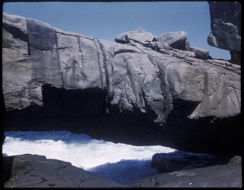 [Rock arch with white-topped waves underneath] [transparency] / [Frank Hurley]