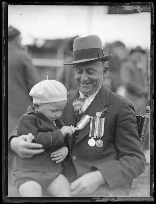 Child playing with the medals of a returned soldier at the ANZAC Day service at Petersham [?], New South Wales, 25 April 1933 [picture]