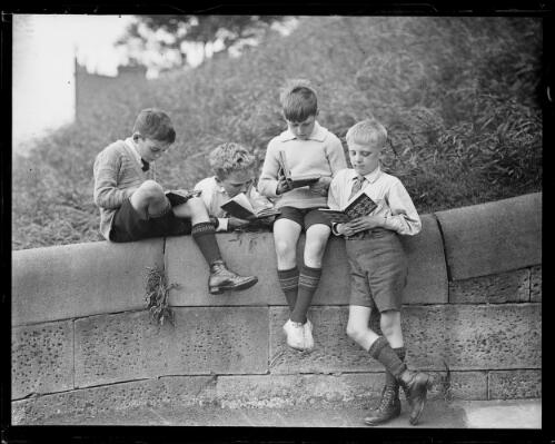 Four young boys reading books on top of a stone wall during health week at school, New South Wales, ca. 1930 [picture]