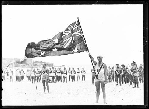 Surf lifesavers carrying the Australian flag during a surf carnival at Bondi Beach, Sydney, 18 March 1933 [picture] / Herbert H. Fishwick