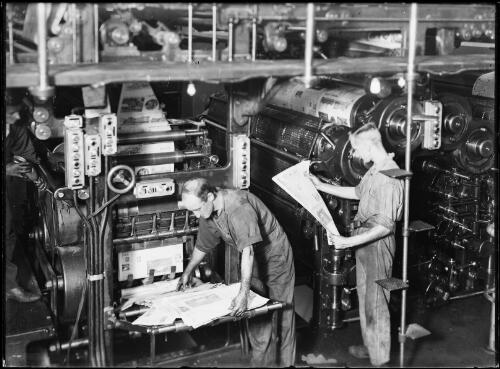 Two men looking at newspapers straight out of the press machinery at the Sun Newspaper, Sydney, ca.1930s [picture]