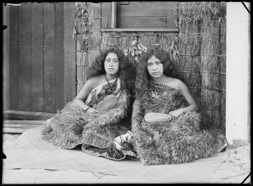Two Maori women in traditional dress sitting on the ground outside a house, New South Wales, ca. 1935 [picture]