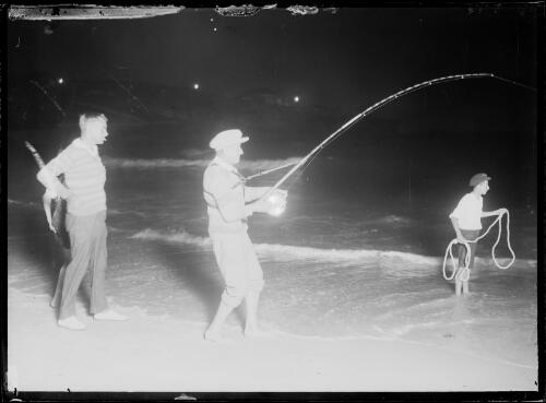 Man watching a fisherman reel in a catch and a young boy holding a rope, New South Wales, ca. 1930s [picture]
