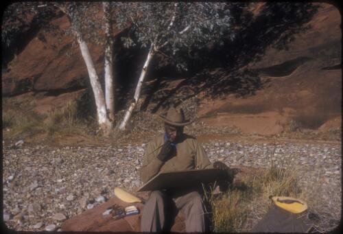 Albert Namatjira painting with artist equipment by his side, Finke River near Hermannsburg, approximately 1953