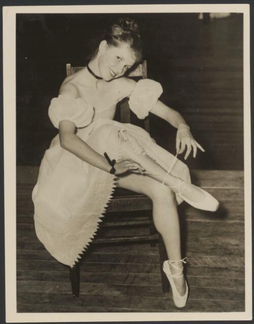 Moya Beaver putting on her pointe shoe, in costume with choker worn in productions of the Lightfoot-Burlakov First Australian Ballet, ca. 1935 [picture]